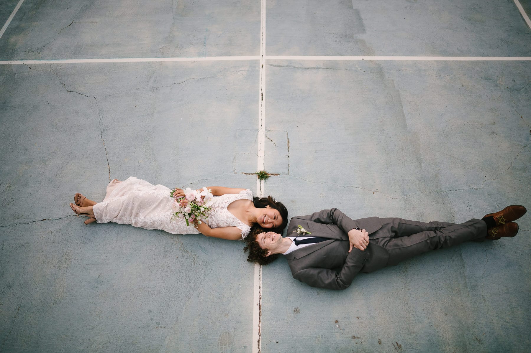 Bride and groom laying on the ground on tennis court at green mountain retreat wedding in los gatos