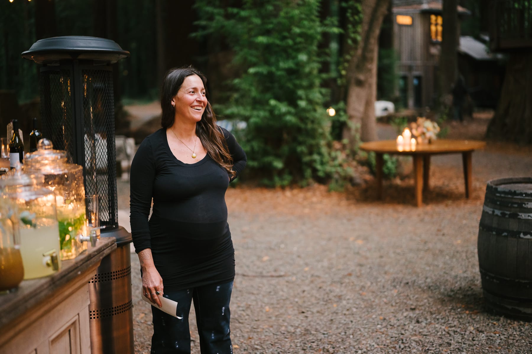 Pregnant event planner, Madeline Hurst, standing near redwoods and portable bar at wedding at the Brambles in Mendocino.
