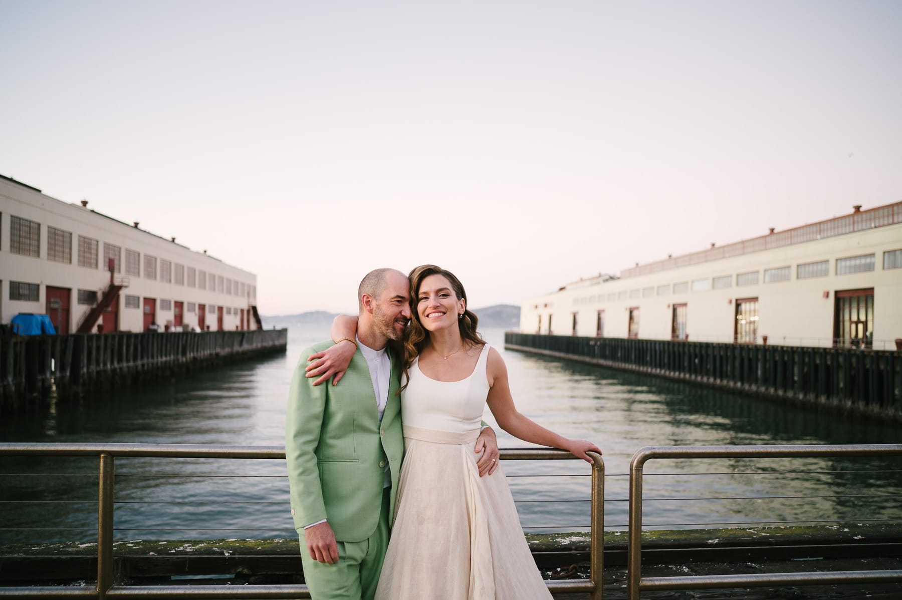Groom in green suit and smiling bride standing in front of the water at Fort Mason wedding