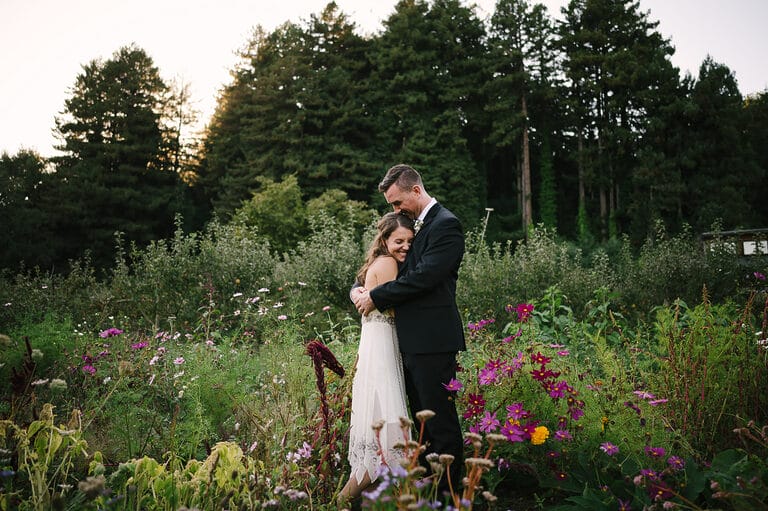 Couple hugging each other in a field of flowers at their wedding at Oz Farm in Mendocino.