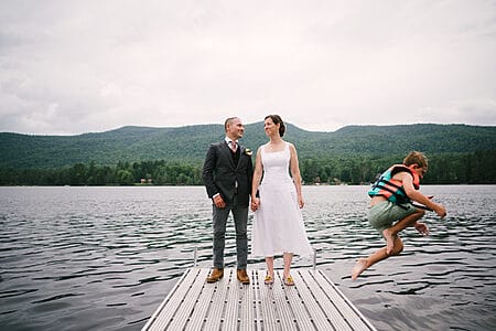 Image of couple standing on dock on lake with kid jumping into water. Part of Bay Area wedding highlights from 2024 from Gabriel Harber Photography.