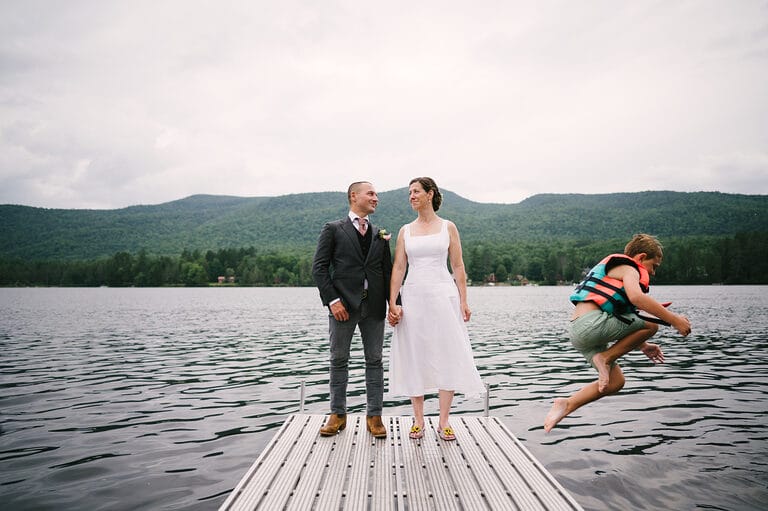 Image of couple standing on dock on lake with kid jumping into water. Part of Bay Area wedding highlights from 2024 from Gabriel Harber Photography.